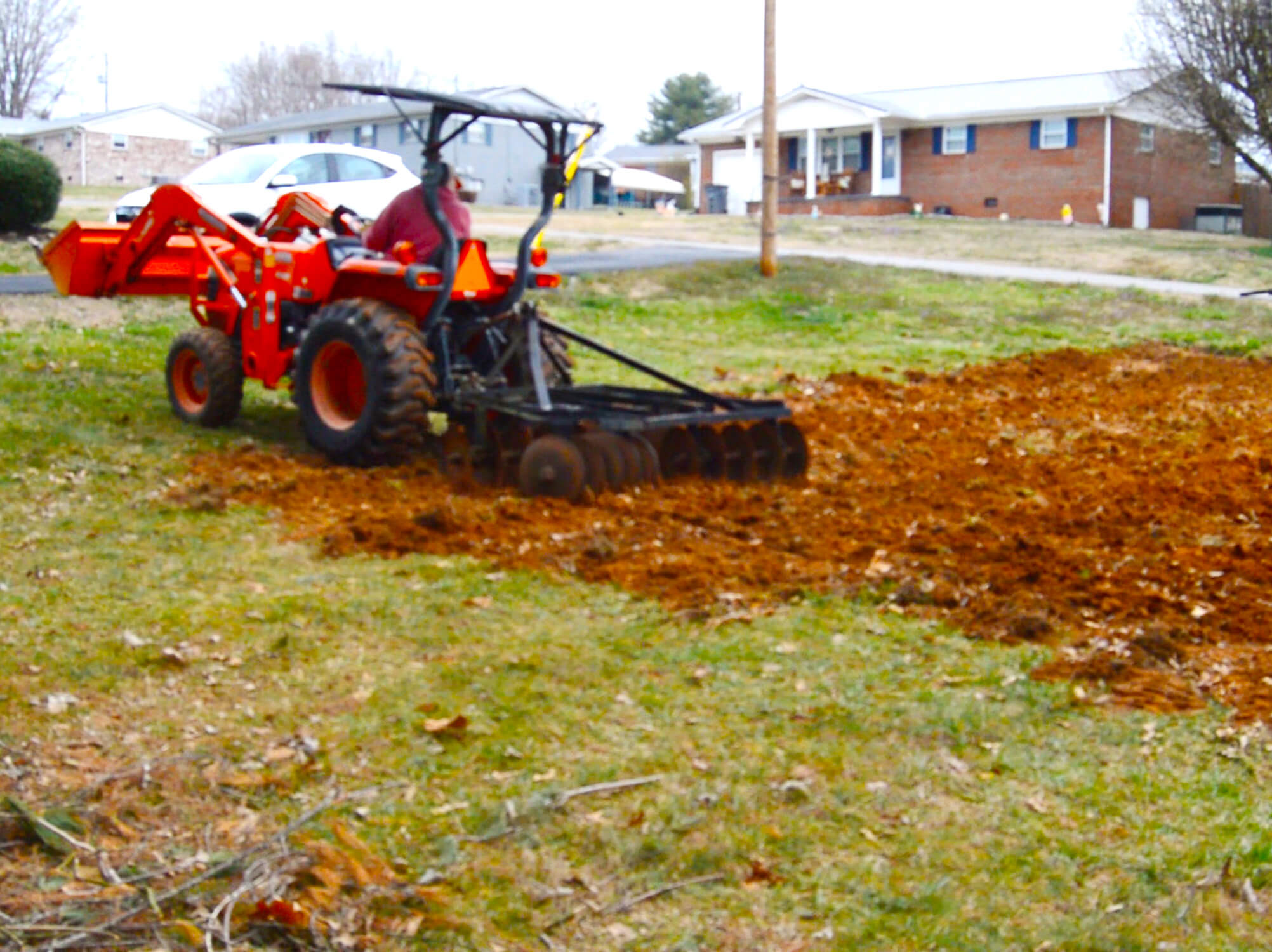 An urban garden being disced by a Kubota subcompact tractor.