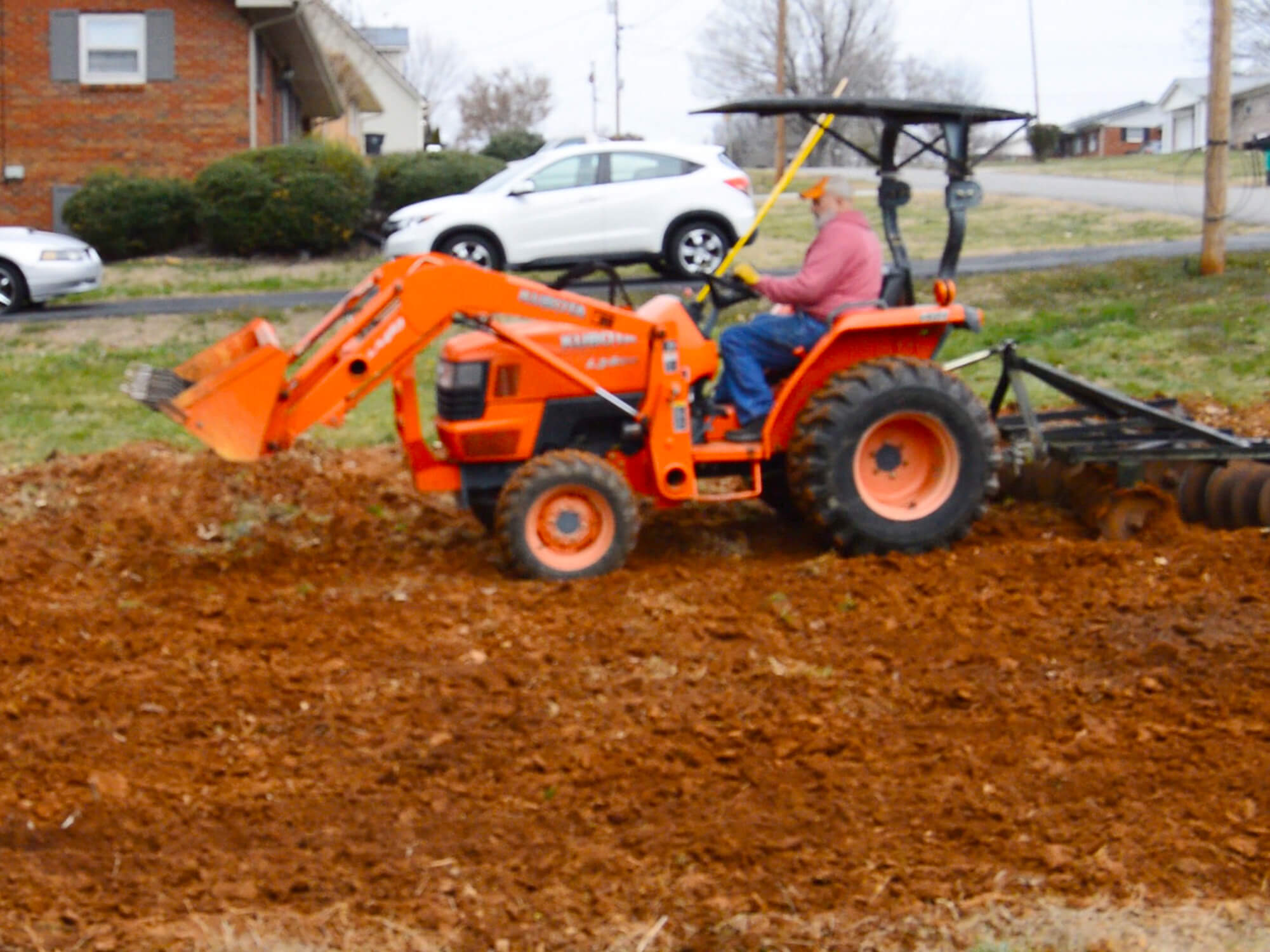 A Kubota subcompact tractor discing an urban garden as an intermediate step between plowing and tilling.